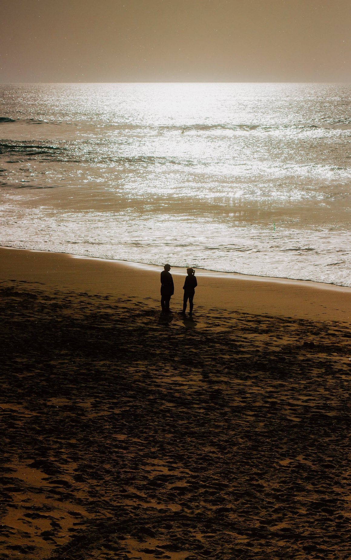 Two silhouettes on a beach against the sea glare